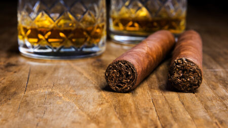 Two Cuban Cigars With Two Glasses Of Whiskey On An Old Wooden Table With A Blurred Background Two Cuban Cigars With Two Glasses Of Whiskey On An Old Wooden Table With A Blurred Background