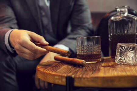 Gentleman Takes A Cigar From A Wooden Table With Carafe Of Whisky And Glass Gentleman Takes A Cigar From A Wooden Table With Carafe Of Whisky And Glass